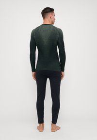 Prilagođena majica s dugim rukavima u tamnozelenoj boji s teksturiranim uzorkom, uparena sa slim-fit crnim hlačama. Minimalistički dizajn, lagani materijal.