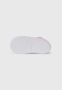 Sole di sneaker bianca con un motivo di trama testurizzato, caratterizzata da un elemento di design circolare e un leggero accento rosa sul bordo.