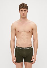 Olivgrüne Boxershorts mit einem schwarzen Bund und weißer Markenbeschriftung. Glattes, elastisches Material, figurbetontes Design ohne Muster.