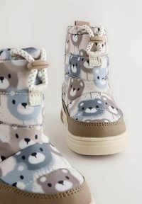 Wasserfeste Kinderstiefel in Hellgrau mit einem Bärenmotiv. Die Merkmale umfassen ein gepolstertes Obermaterial, eine beigen Gummisohle und ein Schnürdesign.