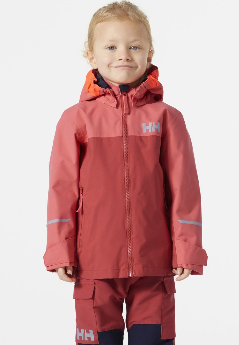 Chaqueta impermeable roja con detalles en naranja, que cuenta con un frente con cremallera, capucha y un logo gris. Combinada con pantalones a juego, también en rojo y azul marino.