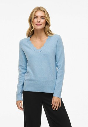 Lichtblauwe v-hals trui met een gegolfde halslijn en geribbelde manchetten. Zachte textuur, getailleerde pasvorm, gecombineerd met zwarte broek. Minimalistisch ontwerp.