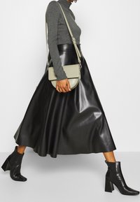 Gonna nera in finta pelle a forma di A, vita aderente, abbinata a un dolcevita grigio e stivaletti neri con tacco. Include una borsa verde a tracolla.