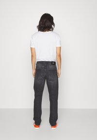 Jeans in denim nero con una vestibilità dritta e cinque tasche. La vista posteriore mostra un'etichetta sulla vita e scarpe arancioni in contrasto.