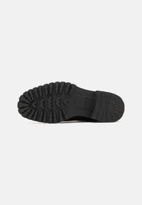 Semelle de botte en caoutchouc noir présentant un motif de crampons robuste avec de profondes rainures et des sections surélevées pour une adhérence optimale. Surface texturée pour une prise en main.