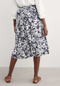 Námořnická květinová sukně s bílým potiskem, ke kolenům, s přiléhavým pasem a skladbami. Nosit s hnědými sandály, které mají hladkou texturu.