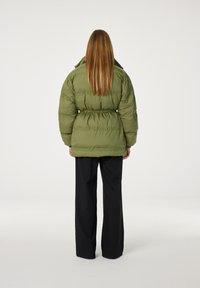 Overmaat groene pufferjack met een getailleerde taille, voorzien van horizontale naden en een hoge kraag. Gecombineerd met zwarte wijde broek.