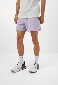 Lila shorts met zijsplits, gecombineerd met witte en paarse sneakers. De outfit wordt aangevuld met witte sokken tot de enkels met een logo.