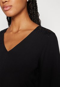 Robe noire avec un décolleté en V et des détails en dentelle sur les épaules. Tissu doux et lisse avec une coupe décontractée.