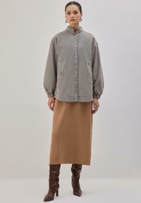 Siva džinsasta prevelika jakna z zapenjalnim gumbom, stranskimi žepi in visokim ovratnikom, kombinirana z rjavo rebrasto midi krilo in rjavimi škornji z visokimi petami.