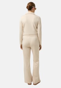 Beżowy top i dopasowane rozszerzane spodnie wykonane z gładkiego, elastycznego materiału. Strój posiada kołnierzyk i dopasowany pas.