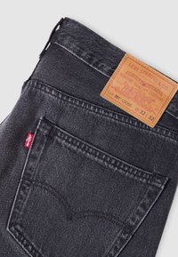 Μαύρο τζιν από denim με καφέ δερμάτινη ετικέτα που φέρει το λογότυπο "Levi Strauss & Co.", διπλή ραφή και πίσω τσέπη με το εμβληματικό σχεδιασμό τόξου.