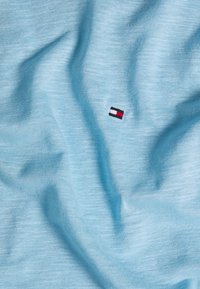 Tela de algodón azul claro con una textura suave, que presenta un pequeño logotipo bordado en rojo, blanco y negro en el lado izquierdo.