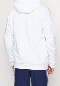 Sweat à capuche blanc avec une poche kangourou, des poignets et un ourlet côtelés. Tissu confortable, doté d'une capuche avec cordon de serrage et d'une texture lisse.