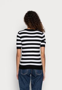 Czarnobiały sweter w paski z krótkim rękawem, wykonany z dzianiny, z prążkowanym dekoltem i ściągaczem, zestawiony z wysokim stanem jeansów.