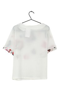 Short-sleeve, white blouse with a round neck; features patterned accents in red, black, and pink on the sleeve hems; smooth texture.