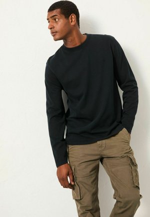 Schwarzes Langarmshirt mit Rundhalsausschnitt, kombiniert mit olivgrünen Cargo-Hosen mit seitlichen Taschen und lockerer Passform.