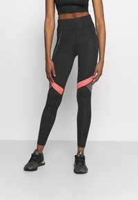Černé legíny s texturovanými vzory, s růžovými síťovinovými akcenty a tvarovaným střihem. V páru s černými sportovními botami.
