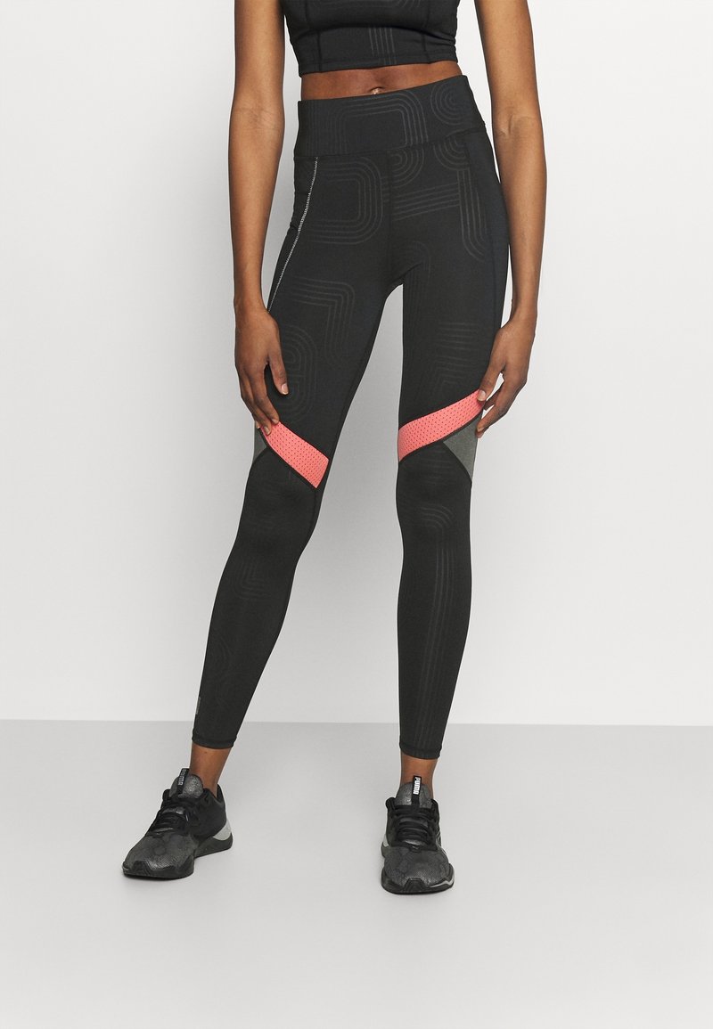 Černé legíny s texturovanými vzory, s růžovými síťovinovými akcenty a tvarovaným střihem. V páru s černými sportovními botami.