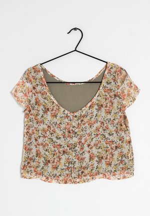 Blouse à manches courtes à motif floral avec des fleurs roses et jaunes, boutonnée devant, suspendue sur un cintre noir sur fond blanc.