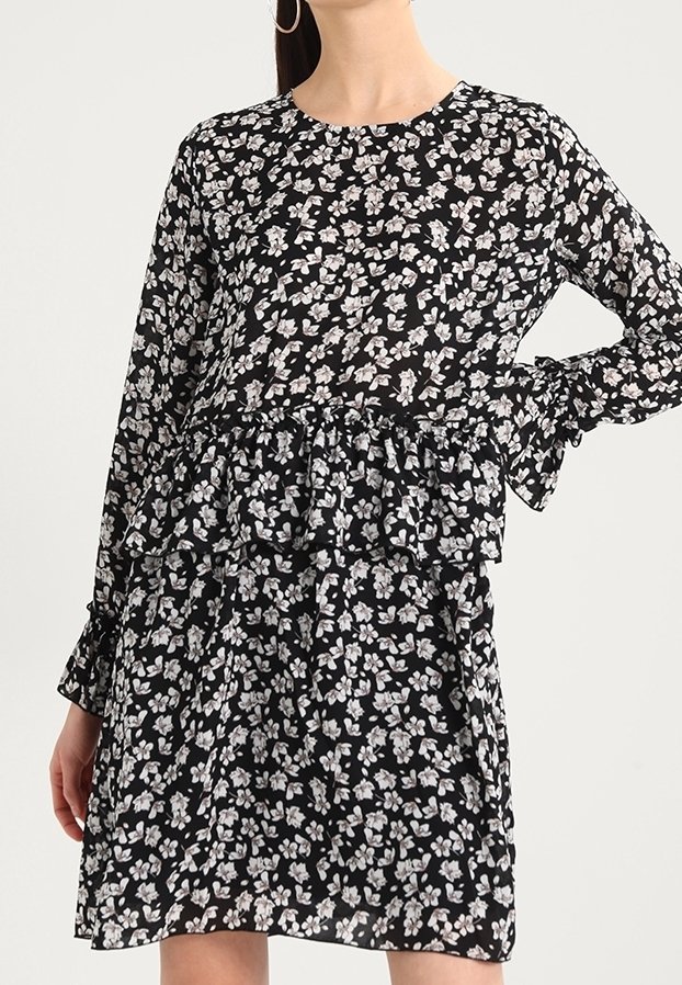 Mustapuku, joka on valmistettu kevyestä kankaasta, jossa on valkoisia ja harmaita kukkakuvioita. Pitkät hihat, röyhelövyötärö ja pyöreä pääntie.