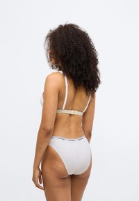 Balts bralets ar regulējamām siksnām un āķa aizdari, kopā ar baltām augstām biksēm, kurām ir logotipa jostasvieta. Lietojams gluds kokvilnas audums.