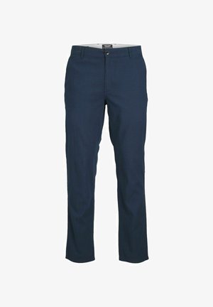 Maglietta henley bianca a maniche lunghe con plastron bottonato; abbinata a pantaloni chinos blu navy e sneakers bianco e nere. Design semplice e casual.