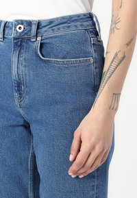 Jeans de mezclilla azul claro con una cintura alta, bolsillos frontales y una textura ligeramente deslavada. Cuenta con un cierre de botón metálico y cremallera.