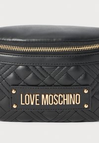Svart, quiltad läderväska med guldfärgad dragkedja och rektangulär platta med texten "LOVE MOSCHINO" i guldiga bokstäver.