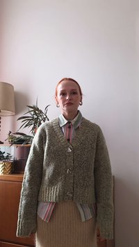 Khakifarbener, grob gestrickter Cardigan mit übergroßen Ärmeln und strukturierter Oberfläche, versehen mit großen Knöpfen. Darunter kombiniert mit einem gestreiften Hemd.