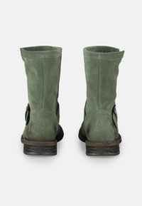 Botines de ante verdes con una suela plana negra, que presentan un detalle de hebilla lateral y un eje recto, ligeramente caído.