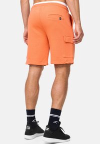 Shorts cargo orange avec taille à cordon, poches latérales et une poche arrière. Fabriqués en tissu doux, présentant une coupe décontractée et longueur genou.