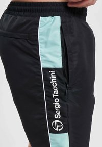 Shorts de sport negri din material ușor, având un panou lateral verde mentă, dotat cu un buzunar cu fermoar și cu un logo alb pe picior.