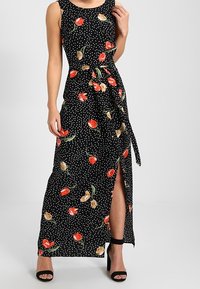 Maxi šaty černé barvy s bílými puntíky, obsahující květinový vzor s červenými tulipány a zelenými listy, a s předním rozparkem. Černé sandály.