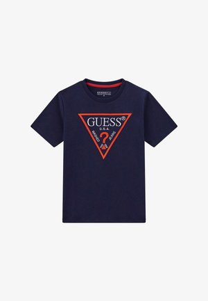 Tumedane sinine puuvillane T-särk lühikeste varrukatega, mille esipooles on punane ja valge kolmnurkne logo koos "GUESS U.S.A." tekstiga.