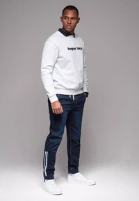 Sudadera en gris claro con el texto "Bonjour Tokyo", combinada con joggers azul marino con rayas blancas y zapatillas blancas.