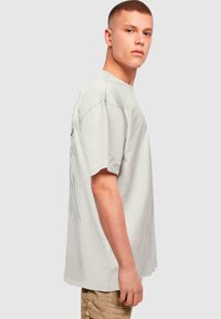 Camiseta de algodón gris claro de ajuste holgado, con un diseño gráfico de alas en la parte posterior. Mangas cortas y estilo de cuello redondo.