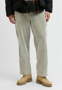 Lys grønne kordfløyelsbukser med vide ben og sidelommer, kombinert med beige støvler. Materialet har en vertikal ribbestruktur.