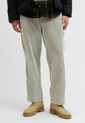 Lys grønne kordfløyelsbukser med vide ben og sidelommer, kombinert med beige støvler. Materialet har en vertikal ribbestruktur.