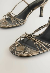 Bälte högklackade sandaler med ett svart och beige snakeskin-mönster, har en elegant design och en öppen tå framtill.