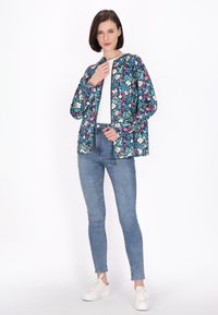 Giacca zip-up floreale in navy, con fiori multicolori. Indossata sopra una maglietta bianca con jeans skinny e sneakers bianche.