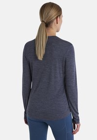 Navyblaues Langarmshirt aus weichem, strukturiertem Stoff mit Rundhalsausschnitt und enganliegenden Ärmeln, kombiniert mit blauen Sporthosen.