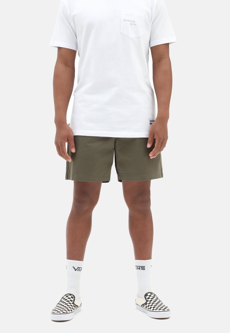 Korte olivengrønne shorts, hvid t-shirt med brystlomme, ternede slip-on sko og hvide sokker med "Vans" branding.