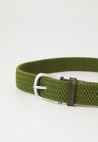 Cinto verde, trançado, feito de material elástico, com uma fivela de metal prateado e uma ponta em couro com uma marca gravada. Acabamento texturizado.