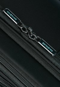 Black fabric zipper bag with metal zipper hardware. Features textured fabric and a silver logo tag on the zipper pull.
