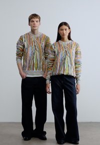 Χρωματιστά, υφασμένα πουλόβερ με στροβιλιζόμενα σχέδια, συνδυασμένα με σκούρα, χαλαρά τζιν. Και τα δύο αντικείμενα διαθέτουν άνετα, χαλαρά σχέδια.