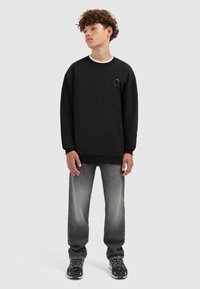 Zwarte sweatshirt met een ronde halslijn en geborduurd detail. Gecombineerd met grijze jeans met een lichte wassing, gedragen met zwarte sneakers.