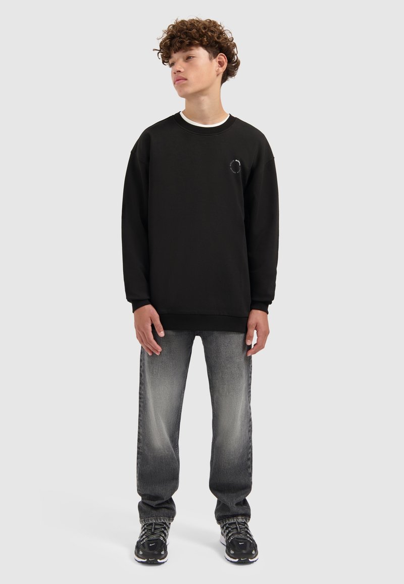 Zwarte sweatshirt met een ronde halslijn en geborduurd detail. Gecombineerd met grijze jeans met een lichte wassing, gedragen met zwarte sneakers.