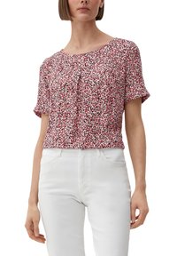 Kurzarmlige, rot-weiße Bluse mit floralem Muster und Falten am Ausschnitt, aus leichtem Stoff; kombiniert mit weißen, hoch taillierten Jeans.