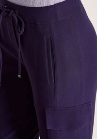 Paarse cargobroek van textuurstof met een drawstring taille, zijzakken en een opgestikte zak op de dij.